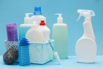 Bottles of dishwashing liquid in basket and brushes on blue background.
