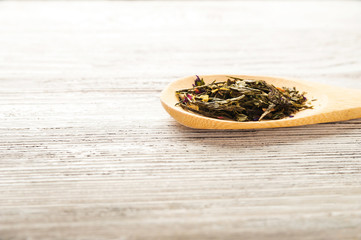 Fototapeta na wymiar Organic natural green tea on a wooden spoon close-up. Brewed tea on a spoon on the background of white textured table and copy space