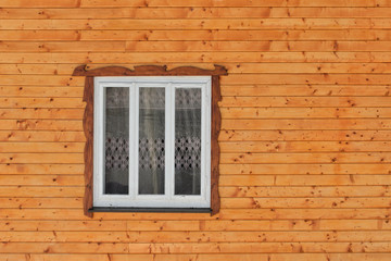 White wooden window in the wall of raw brown wooden planks with knots. Frontal view. Close-up.