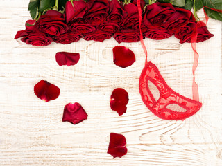 Romantic carnival concept. Red carnival mask and bouquet of red roses on light wooden background. Top view