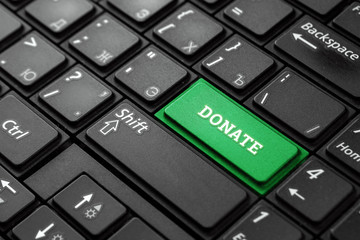 Closeup of a green button with the word Donate, on a black keyboard. Creative background, copy space. Concept magic button, investor, salary, blogger, blood donation, homeless, charity.