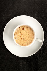 An overhead photo of a cup of coffee with foam on a black background with copy space