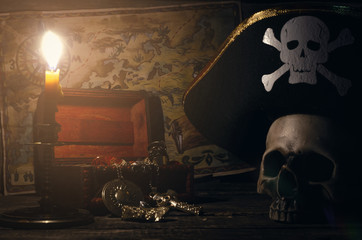 Pirate map and treasure chest with a gold and human skull in captain hat on a pirate captain table...