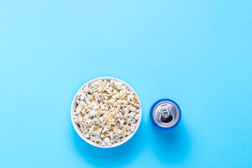 Bowl with popcorn and a can of drink on a blue background. The concept of watching movies and favorite TV shows, sports competitions. Flat lay, top view
