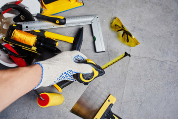 The concept of repair. Male hand holding a tape measure against a background of construction tools. First person view.