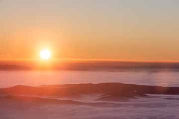 Obraz premium Beautiful sunset over a valley filled by fog with mountains and hills