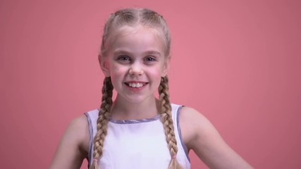 Smiling girl with braids having fun, closing eye with heart-shaped lollipop