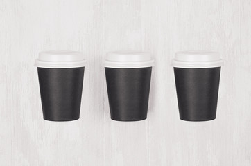 Coffee mockup - set of three  blank black paper cups with white caps on white wood board, top view. Modern elegant concept for branding identity, advertising, design.