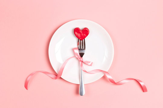 Fork with a heart on a plate on a pink table. Festive menu for Valentine's Day. T