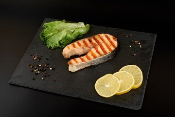 Grilled salmon steak with a lemon and salad on a slate plate.