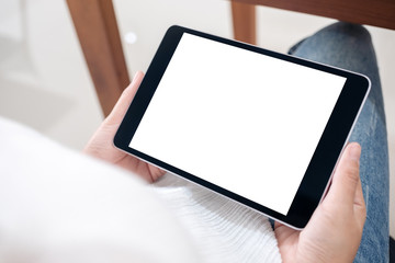 Mockup image of a woman holding black tablet pc with blank white screen horizontally while sitting in cafe