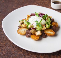 Warm salad with chicken, grilled potatoes, crackers, arugula, grated cheese and poached egg on a white plate and soy dressing. Close up. Selective focus. The concept of the menu.