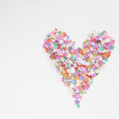Heart of colorful confetti on white background, concept of Valentine's day. Close up. Top view.