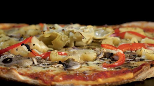 A freshly baked pizza with lots of vegetables and cheese rotates in close-up