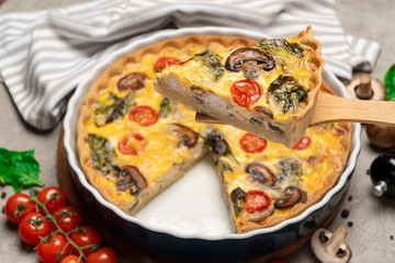 Baked homemade quiche pie in ceramic baking form and slice on wooden paddle