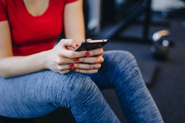 young fit woman holding phone and sending text message taking a break in the gym