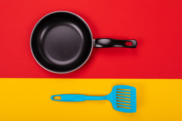 Top view of empty kitchen frying pan with spatula isolated on red-yellow background