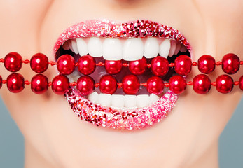 Red lips and white healthy teeth with bright pearls closeup. Perfect female smile with glitter lipstick makeup