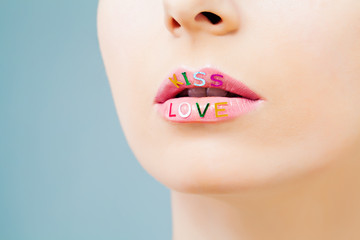Closeup portrait of perfect pink lips with love symbol on blue background. Female lip with bright creative makeup
