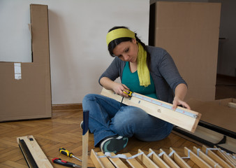 Beautiful women sitting on the floor and measuring peace of flat pack furniture - Image