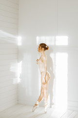 ballet and dance concept. Portrait of a young ballerina girl in a body beige bodysuit. Woman dancing and posing in a bright interior. Stretching, grace and flexibility.