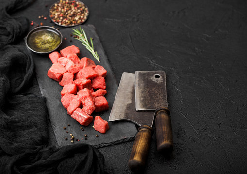 Raw lean diced casserole beef pork steak on chopping board with vintage meat hatchets on stone background. Salt and pepper with fresh rosemary.Space for text