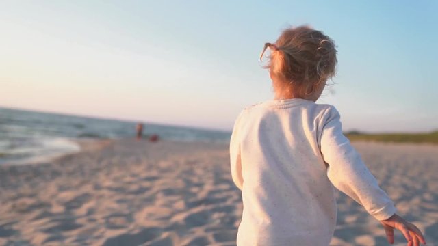 Happy little girl running on the beach in sunset time. Slow motion footage.
