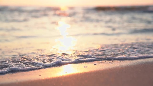 Sunset on the beach. Slow motion footage of sea waves and foam. Sun reflecting on the water surface.