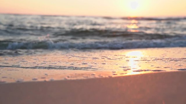 Sunset on the beach. Slow motion footage of sea waves and foam. Sun reflecting on the water surface.