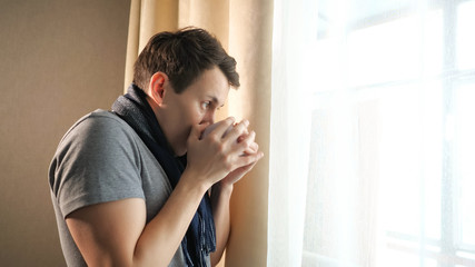 Fototapeta na wymiar Sick male with mug coughing near window