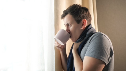 Fototapeta na wymiar Sick male with mug coughing near window