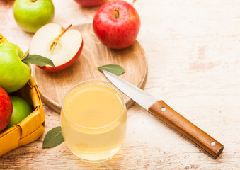 Glass of fresh organic apple juice with red apples on chopping board on wooden background with knife