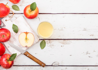 Glass of fresh organic apple juice with red apples on chopping board on wooden background with knife