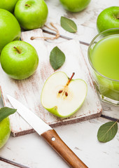 Glass of fresh organic apple juice with green apples on wooden background with knife