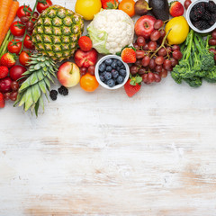 Healthy rainbow fruits vegetables berries, strawberries oranges plums grapes broccoli cauiliflower mango persimmon pineapple on white wooden table, top view, copy space, square