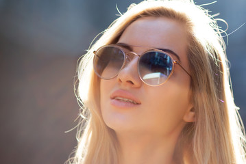 Beautiful young girl with long hair wearing glasses, posing at the street in sunny day. Copy space