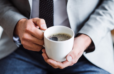 A midsection of businessman sitting in an office, holding a cup of coffee.
