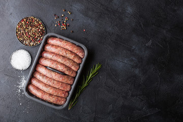 Raw beef and pork sausage in plastic tray with salt and pepper on black background. Space for text