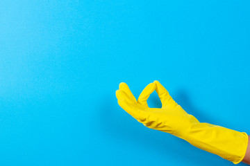 Woman hand with yellow rubber glove making a gesture meaning ok, top view on blue background