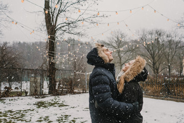 Smiling couple having fun on street near tree with fairy lights