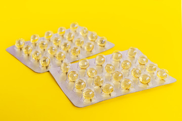 Two blisters with capsules of an oil solution of vitamins A and E on a yellow background close up. Two packs of vitamins or pills. Concept of health care and pharmaceuticals.