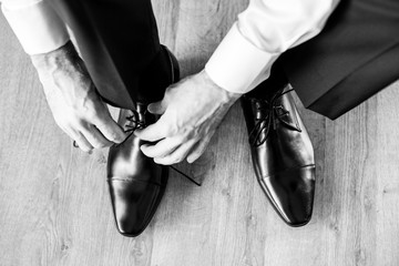 Business man dressing up with classic, elegant shoes. Groom wearing shoes on wedding day, tying the laces and preparing. Black and white photo