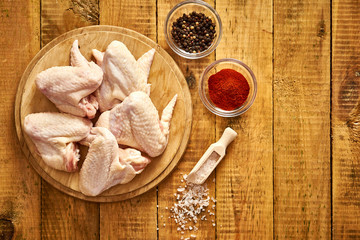 Fresh organic chicken wings on chopping board with chili pepper and salt on wooden table.