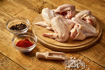 Fresh organic chicken wings on chopping board with chili pepper and salt on wooden table.