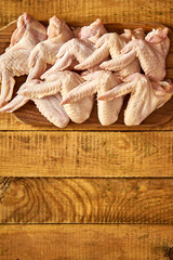 Fresh raw organic chicken wings on chopping board on wooden table.