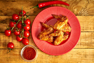 Delicious grilled chicken wings on red plate with spices and tomatoes and chilly peppers on table.