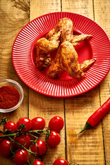 Fototapeta na wymiar Delicious grilled chicken wings on red plate with spices and tomatoes and chilly peppers on table.