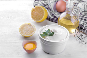 Mayonnaise in a white bowl and ingredients for making mayonnaise on a white wooden background....