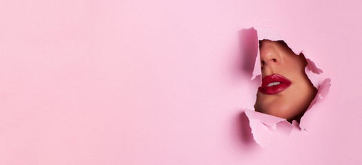View of bright lips through hole in pink paper background. Make up artist, beauty cosmetics sale. Spring, woman day concept. Beauty salon advertising banner with copy space