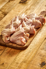 Fresh raw organic chicken wings on chopping board on wooden table.